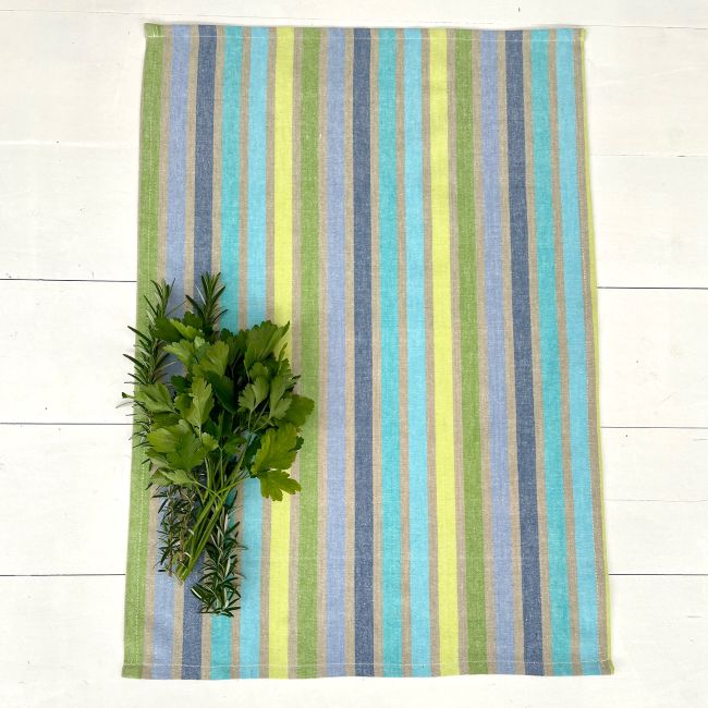 Colorful striped towel with green herbs on a white wooden surface