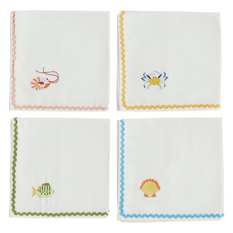 Four white napkins with embroidered sea-themed designs on a white background.