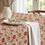 Floral patterned tablecloth on a table with a vase and plates.
