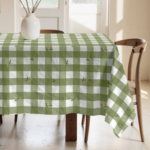 Green and white checkered tablecloth on a wooden table with chairs in a bright room.
