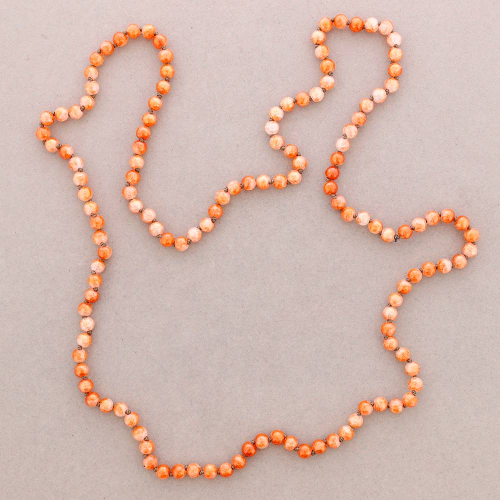 A beaded necklace arranged in an irregular outline on a plain light gray background. The beads are primarily orange with white marbled or speckled sections throughout.