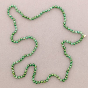 A single strand of small round green beads arranged in a loose loop on a plain light taupe background.
