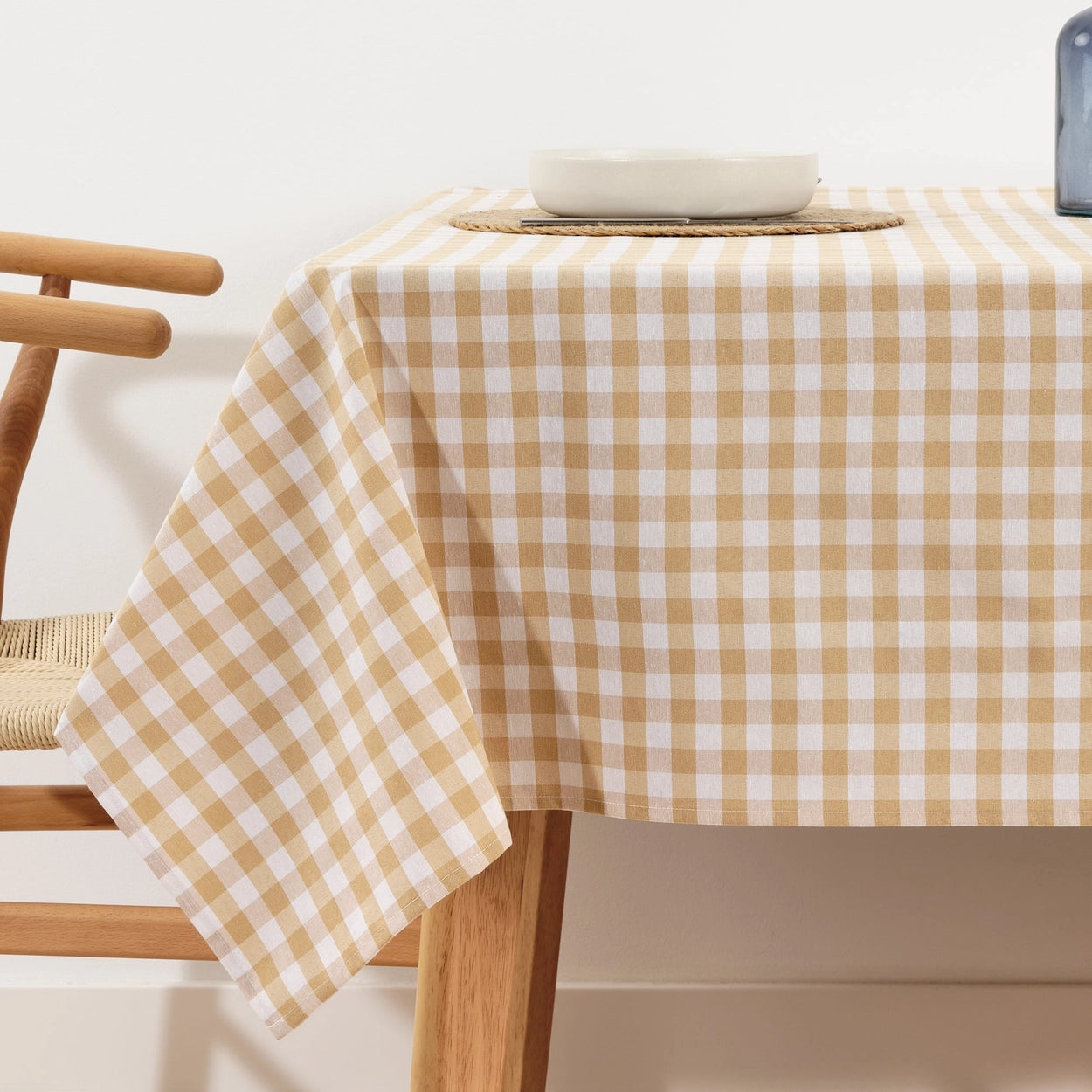 Table with a beige and white checkered tablecloth, wooden chair, and white bowl on a light background