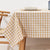 Table with a beige and white checkered tablecloth, wooden chair, and white bowl on a light background