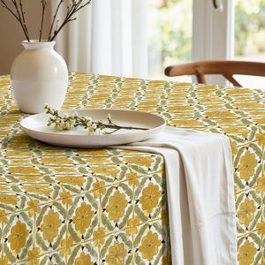 Table setting with a floral patterned tablecloth, white plates, and a vase.