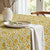 Table setting with a floral patterned tablecloth, white plates, and a vase.