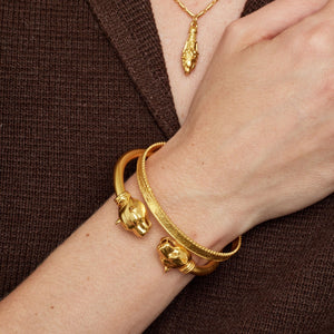 Gold bracelets on a wrist against a brown background