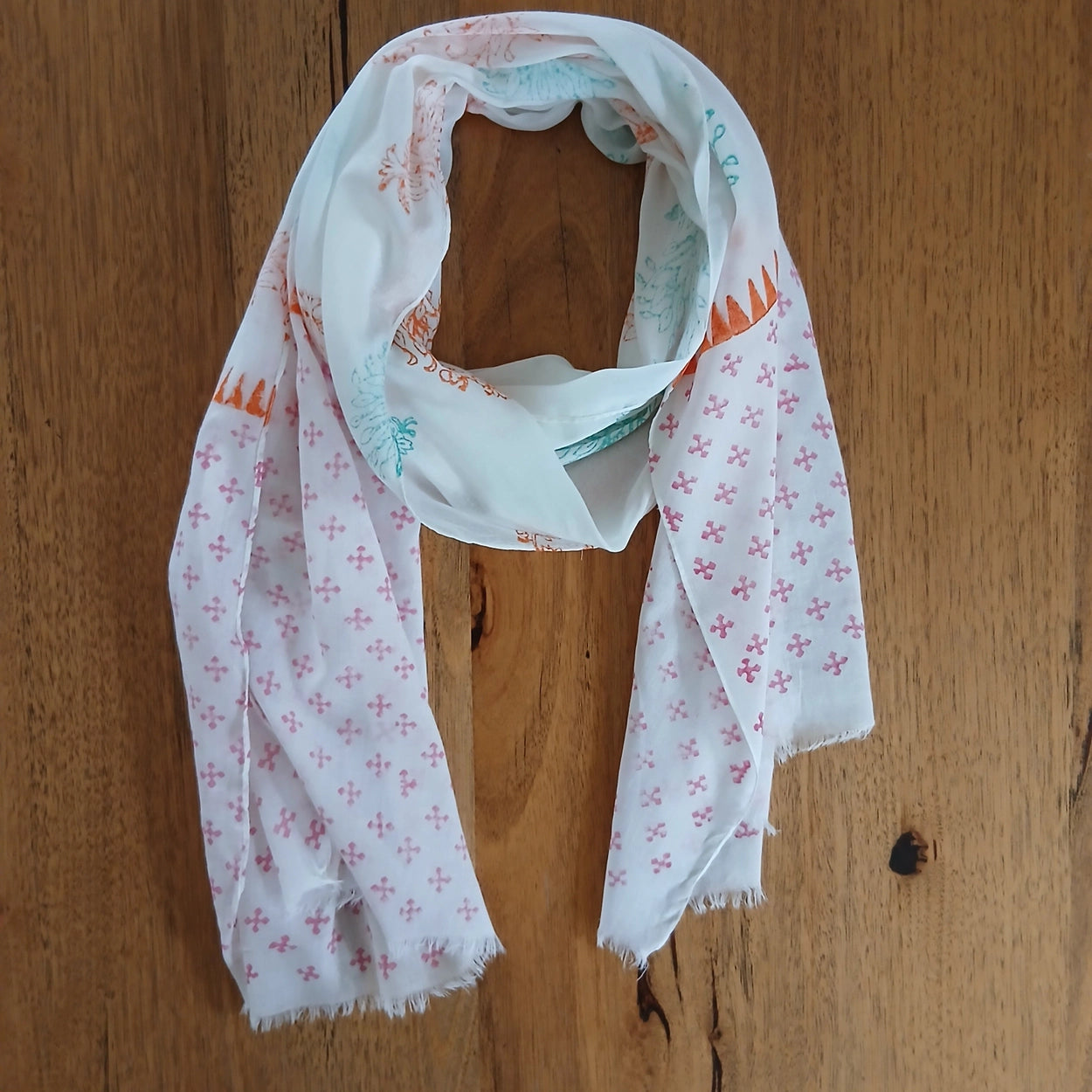 White scarf with pink, orange and green floral patterns draped over a wooden surface