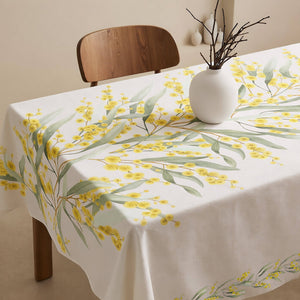 Tablecloth with yellow floral design on a table with a vase.