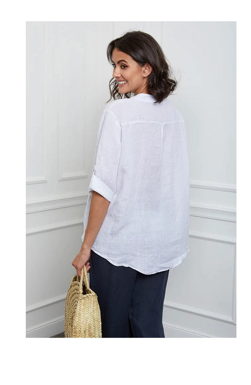Woman wearing a white shirt and  pants holding a straw bag against a white wall.
