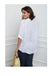 Woman wearing a white shirt and holding a straw bag against a white wall