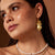 Close-up of a woman wearing gold earrings with a brown background