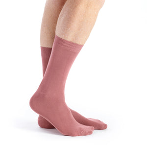 A pair of dusty rose crew socks worn on a person's feet, shown against a plain white background.