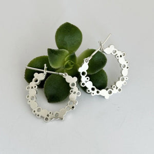 Silver hoop earrings with intricate designs on a light gray background with a green succulent plant.