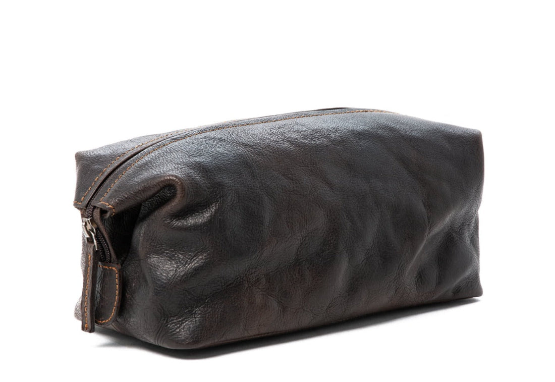 Three leather toiletry bags in brown, black, and cognac on a white background