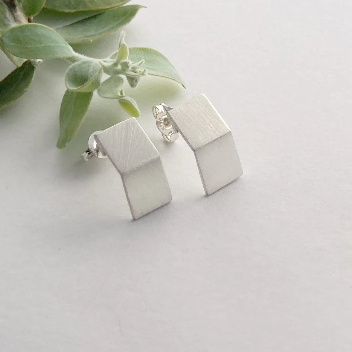 Silver geometric earrings on a light background with green leaves.
