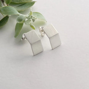 Silver geometric earrings on a light gray surface with green leaves.