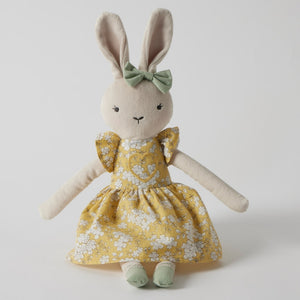Stuffed bunny toy in a yellow dress with a green bow on a white background