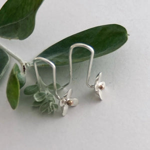 Silver earrings with floral designs on a light gray background with green leaves.